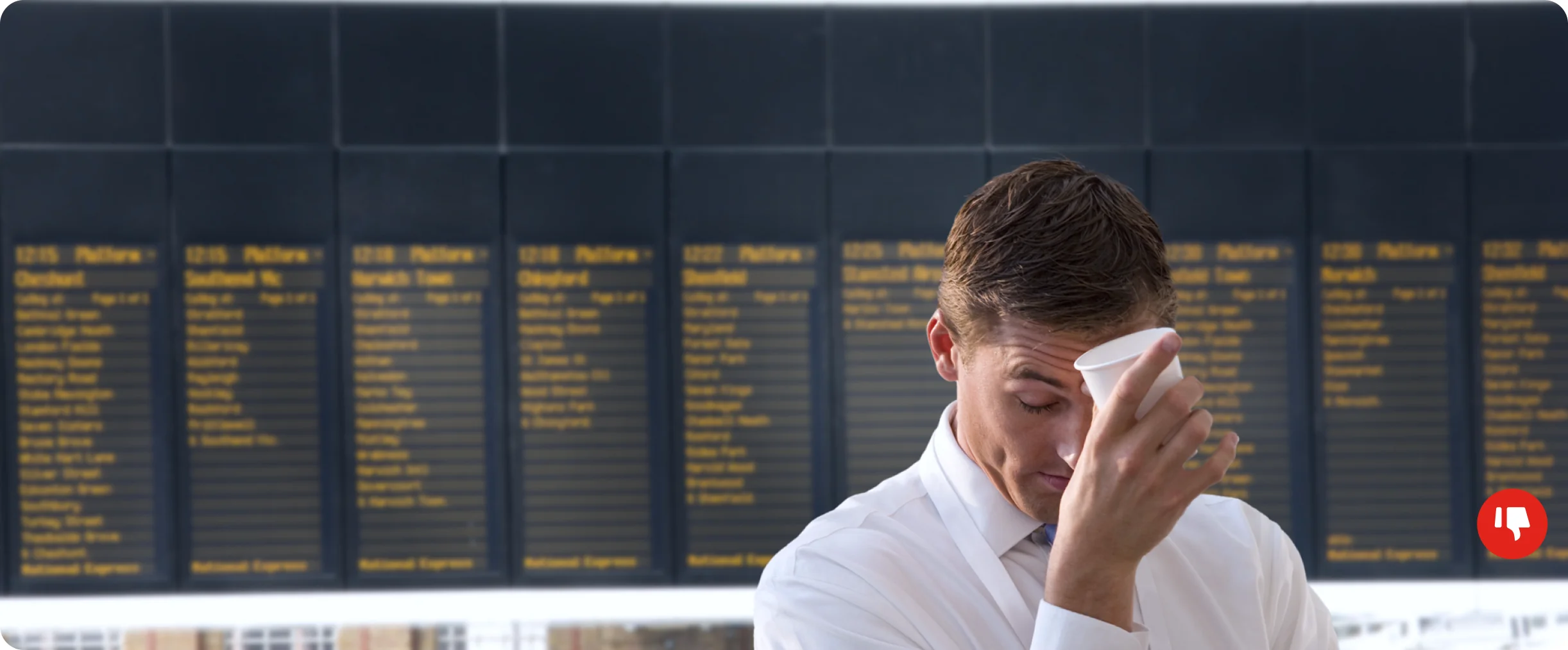 A tired traveler holding a paper cup to his forehead in front of a departures board